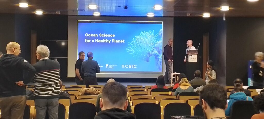 Title slide of a presentation "Ocean Science for a healthy planet", projected on a screen. A conference room with scientists.